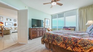 Un dormitorio amplio con una cama grande, ventilador de techo, televisor y balcón con vistas.