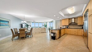 A spacious kitchen with modern appliances, a dining area with wicker chairs, and large windows offering a view.