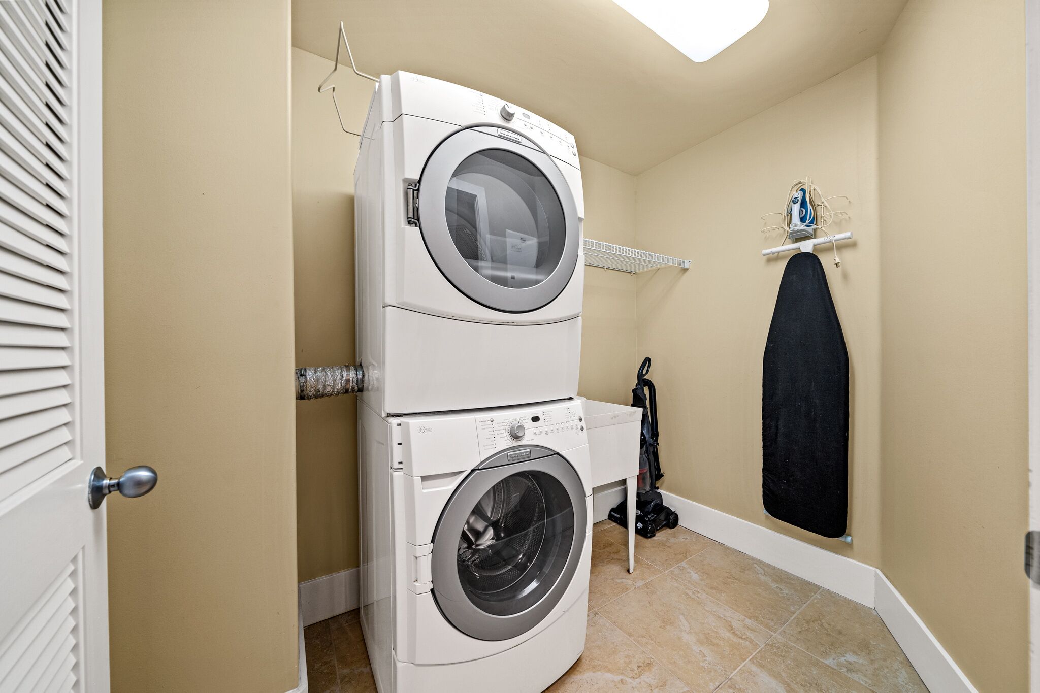 A laundry room with two stacked washing machines, a drying rack, and a vacuum cleaner.
