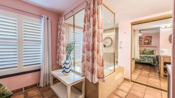 Habitación de hotel con un espejo grande, una consola con un jarrón, una planta en maceta y vistas al baño.