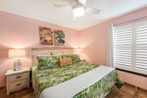 Ein Schlafzimmer mit Bett, Nachttischen, Deckenventilator und Kunstwerken an der Wand.