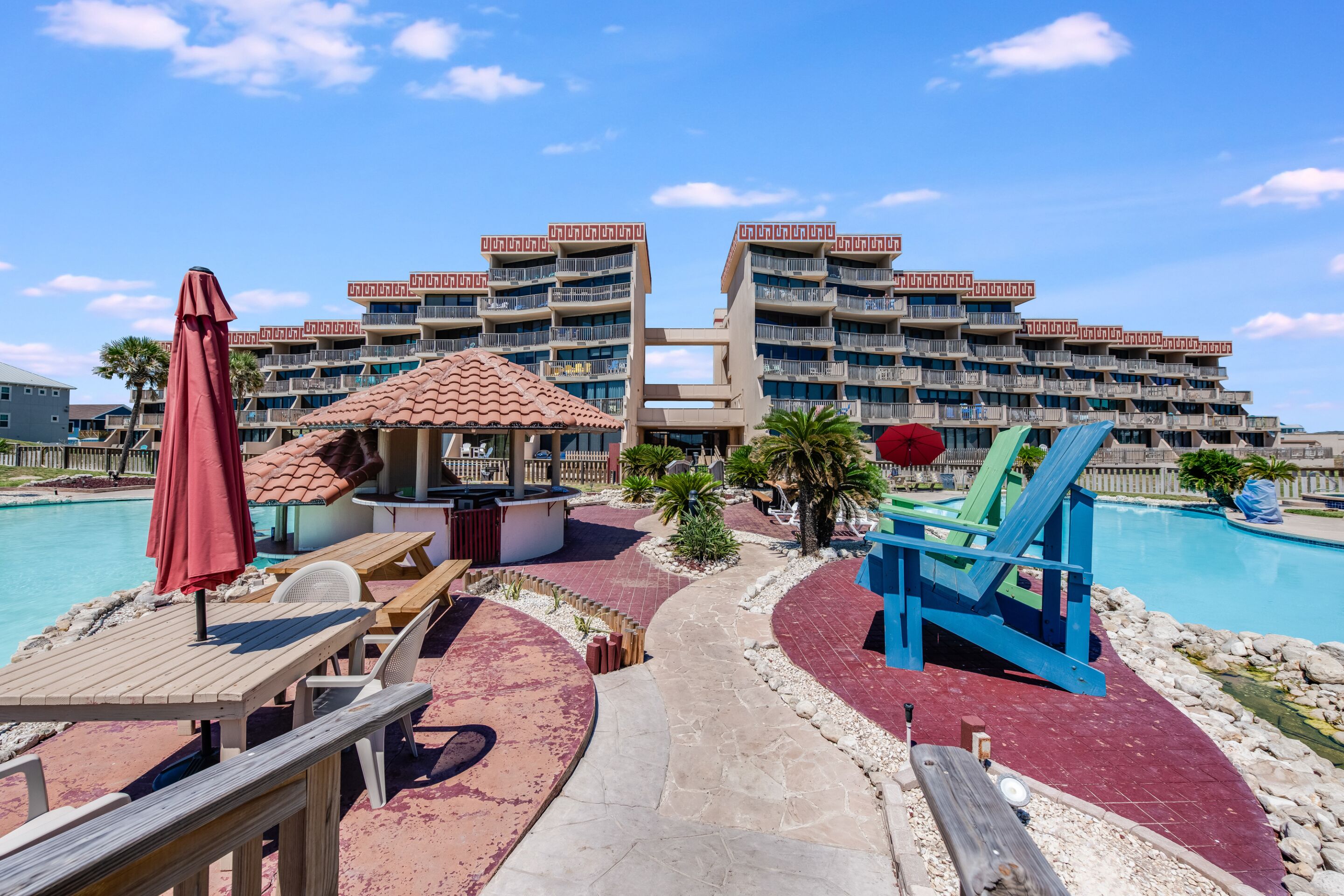 A resort with a pool, outdoor seating, and a multi-story building with balconies.