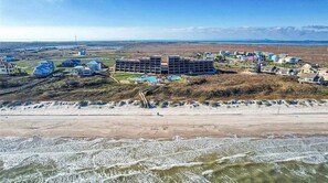 An aerial view of a coastal hotel with multiple buildings, a beach in the foreground, and a clear sky. - Beachfront 2/2 Mayan Princes King + queen, 75" TV (Port Aransas)