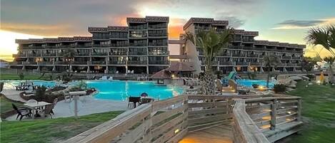 A hotel with multiple balconies overlooking a pool area, a wooden deck, and a sunset view.