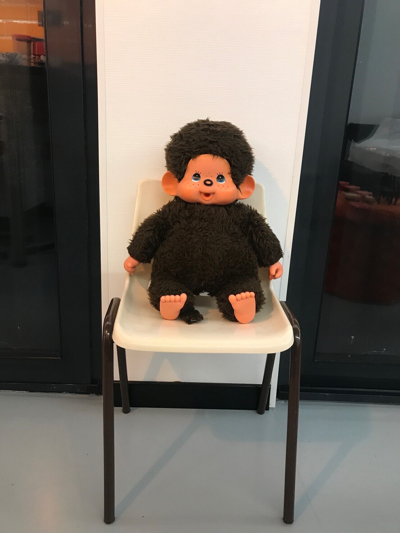 A plush toy seated on a white chair with a black frame.