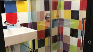 A bathroom with a glass shower enclosure, a white sink, and a colorful tiled wall. - Unusual accommodation la kischte (COLMAR)