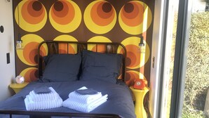 A bed with a dark headboard, a wall with a circular pattern, and a window with a view of greenery. - Unusual accommodation la kischte (COLMAR)
