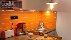 A kitchen with orange tiles, a coffee maker, a toaster, and a sink. - Unusual accommodation la kischte (COLMAR)