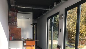 A modern kitchen with a built-in oven, a dining area with a red bench, and large sliding glass doors leading to a garden. - Unusual accommodation la kischte (COLMAR)