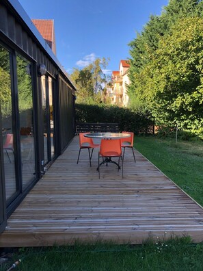 A wooden deck with a table and chairs, surrounded by greenery and a building with large windows. - Unusual accommodation la kischte (COLMAR)