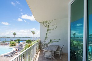 Un balcón con vista al mar, una piscina y sillones de descanso.