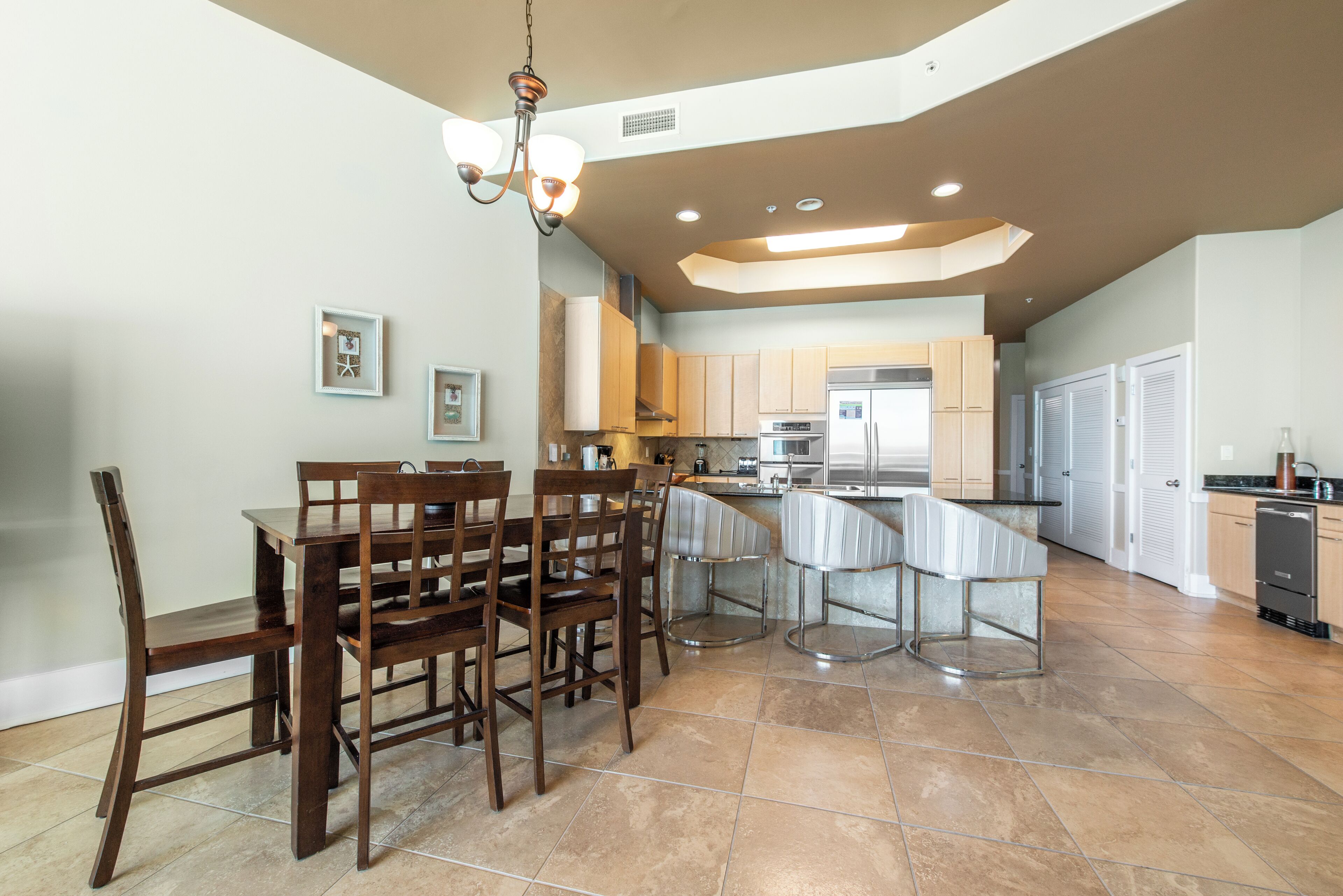 A spacious kitchen with modern appliances, a dining area with wooden chairs, and a chandelier.