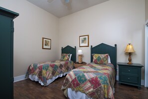 A room with two beds, each with a quilted bedspread, a nightstand with a lamp, and a framed picture on the wall.
