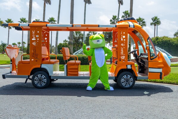 A mascot in a green frog costume standing next to a vehicle with a ladder and orange seats. - Charming Amenity Level Condo with Smart TV and Easy Pool Access. Complimentary Boat Slip! (Orange Beach)