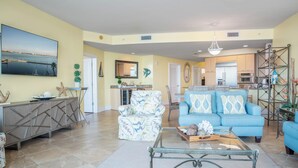 A spacious living area with a large TV, a blue sofa, and a dining area with a buffet table. - Three Bedroom Condo with Calming Bay Views! Complimentary Boat Slip! Message about Spring Special (Orange Beach)