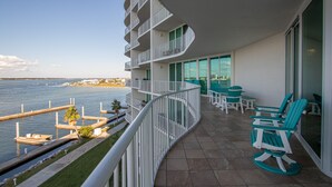 Een balkon met een gebogen reling dat uitkijkt over een jachthaven. Er staan groene stoelen en een kleine tafel.