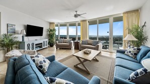 A spacious living room with a large TV, comfortable sofas, a coffee table, and a balcony with a view.