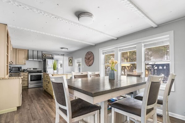 A modern kitchen with stainless steel appliances, a dining area with a large table and chairs, and a view of the outdoors through large windows.