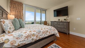 Quarto com uma cama grande, televisão, cômoda e vista para o exterior.