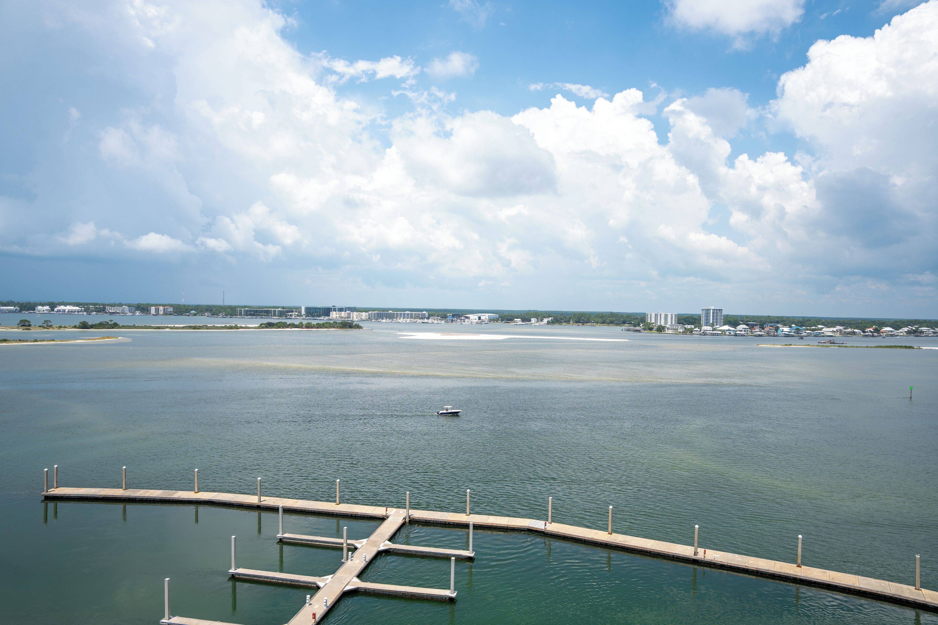 A marina with docks and a boat in the water, surrounded by buildings and a clear sky.