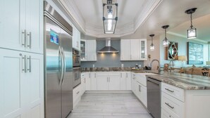 A modern kitchen with white cabinetry, stainless steel appliances, a marble countertop, and pendant lighting.
