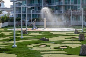 Un jardin aménagé avec une fontaine, des piliers blancs et un bâtiment doté de balcons en arrière-plan.