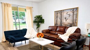 A living room with a blue sofa, a brown leather sofa, a white coffee table, and a painting on the wall. - Resort Villa, Pools Fun and relaxation/w Kingbed. (Kissimmee)