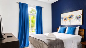 A bedroom with a bed, blue curtains, a painting, and a desk. - Resort Villa, Pools Fun and relaxation/w Kingbed. (Kissimmee)