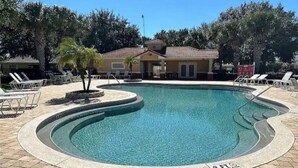 A swimming pool with a curved edge, surrounded by lounge chairs and a building in the background. - Resort Villa, Pools Fun and relaxation/w Kingbed. (Kissimmee)