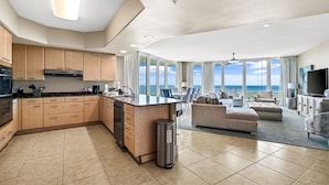 A spacious living area with a large window overlooking the ocean, a kitchen with wooden cabinets, and a modern ceiling design.