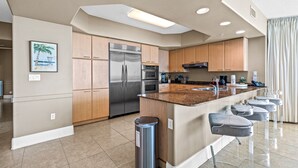 A modern kitchen with a central island, stainless steel appliances, wooden cabinets, and a bar area with stools.