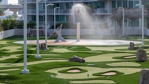 A landscaped garden with a fountain, white columns, and a building with balconies in the background.