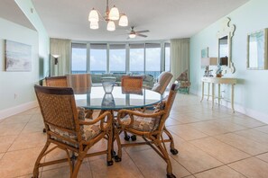 Un comedor amplio con una mesa redonda de cristal rodeada de sillas de mimbre, ventanas grandes con vistas y un ventilador de techo.