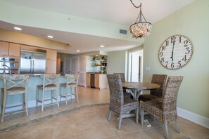 A spacious kitchen with modern appliances, a dining area with wicker chairs, and a large wall clock.