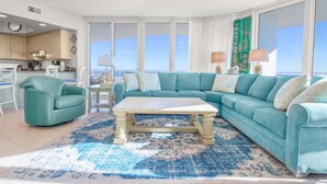 Ein Wohnzimmer mit einem türkisfarbenen Sofa, einem Couchtisch und Meerblick durch große Fenster.