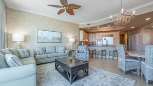 A spacious living room with a gray sofa, a coffee table, and a dining area with wicker chairs and a wooden table. - Relaxing Two Bedroom Penthouse with Gulf and Bay Views! Complimentary Boat Slip! (Orange Beach)