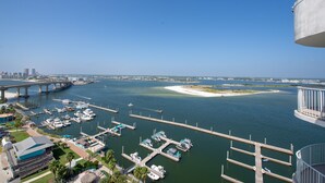A marina with boats docked, a bridge in the background, and a clear view of the water. - Relaxing Two Bedroom Penthouse with Gulf and Bay Views! Complimentary Boat Slip! (Orange Beach)