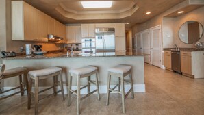 A modern kitchen with wooden cabinets, a central island with stools, stainless steel appliances, and a large window above the island. - Relaxing Two Bedroom Penthouse with Gulf and Bay Views! Complimentary Boat Slip! (Orange Beach)