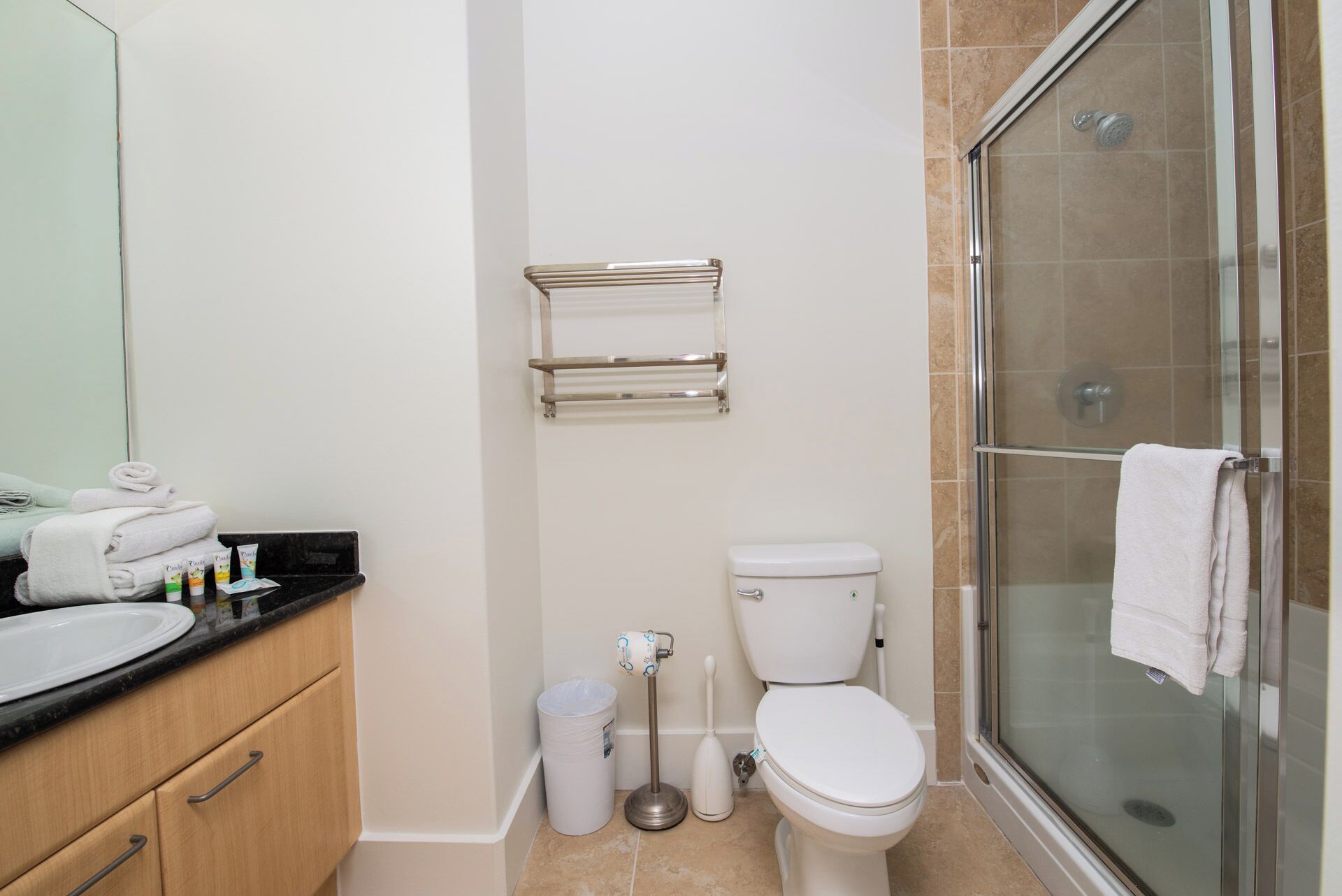 Un baño con inodoro, cabina de ducha de vidrio, lavabo con artículos de aseo y toallero.