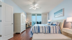 Une chambre à coucher avec un lit, un ventilateur de plafond, une commode, une chaise et une vue sur l’extérieur.