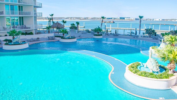 A large outdoor swimming pool with a circular design, surrounded by palm trees and lounge chairs.