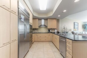 A modern kitchen with stainless steel appliances, light wood cabinets, and a black countertop.