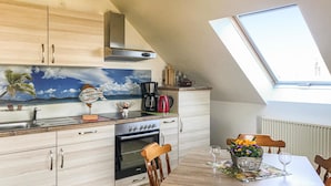 Une cuisine moderne dotée d’une verrière, d’un tableau représentant une scène de plage et d’un coin repas avec une table mise pour deux personnes.