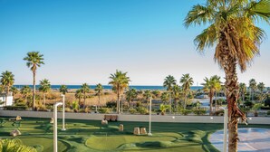 Ein Golfplatz mit freiem Blick auf den Ozean, Palmen und einem gepflegten Grün.