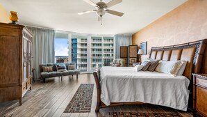 A spacious bedroom with a large bed, a ceiling fan, a view of the city, and a balcony with a view of the buildings. - Spacious and Cozy Two Bedroom Condo with Pool View! Complimentary Boat Slip! (Orange Beach)