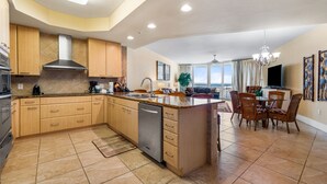 A spacious kitchen with wooden cabinets, a central island, and a dining area with wicker chairs. - Spacious and Cozy Two Bedroom Condo with Pool View! Complimentary Boat Slip! (Orange Beach)