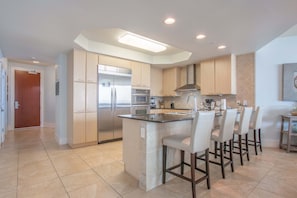 A modern kitchen with a central island, bar stools, stainless steel appliances, and recessed lighting.