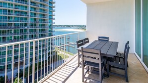 A balcony with a table and chairs, overlooking a beach and a high-rise building. - Updated Family-Friendly Condo with Media Room and Wraparound Balcony. Complimentary Boat Slip! (Orange Beach)