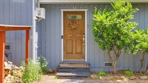 Une maison avec une porte d’entrée en bois, un petit porche et un arbre devant.
