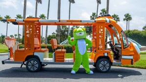 A mascot in a green costume standing next to an orange fire truck.